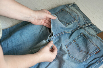 Female hands with old torn jeans spread out on the table. The concept of clothing repair, recycling, home hobbies and work at home