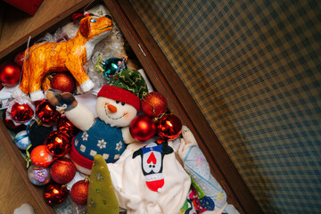 High-angle view of various festive Christmas toys and colorful balls lying in old family suitcase box, selective focus. Preparing for xmas, new year and winter holidays, happy mood.