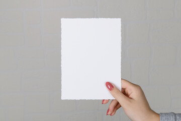 Woman hands holding blank paper sheet A5 size or letter on grey wall background. Close up of 5x7...