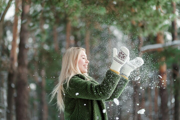 Pretty young blond woman, dressed warmly, with a scarf and mittens. Beautiful girl having fun in...