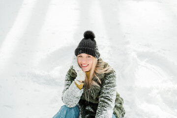 Pretty young blond woman, dressed warmly, with a scarf and mittens. Beautiful girl having fun in the snow