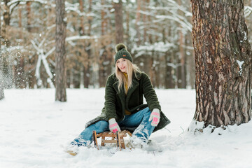Fototapeta na wymiar Beautiful young girl enjoying winter outdoors. Pretty women having fun with snow and sled in forest or park.