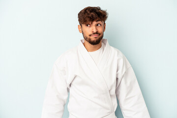 Young mixed race man doing karate isolated on blue background confused, feels doubtful and unsure.