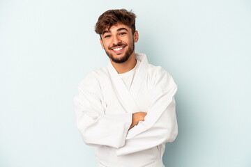 Young mixed race man doing karate isolated on blue background laughing and having fun. © Asier