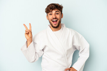 Young mixed race man doing karate isolated on blue background joyful and carefree showing a peace symbol with fingers.