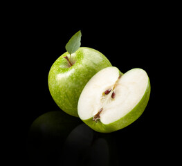 Manzana verde entera y cortada con hoja sobre fondo negro. Whole and cut green apple with leaf on black background.