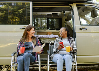 Delighted multiracial travelers relaxing near camper in woods