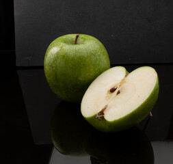 Manzana verde entera y cortada sobre fondo negro, fruta del  mercado.  Whole and cut green apple on black background, market fruit