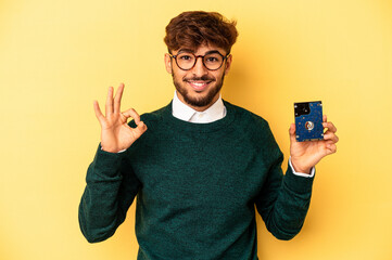 Young computerizer man isolated on yellow background cheerful and confident showing ok gesture.
