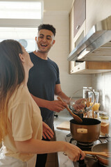 Cheerful young couple enjoying cooking dinner together at kitchen counter