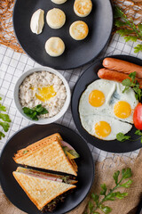 American breakfast with toast, cheese cakes, oatmeal and fried eggs with sausages