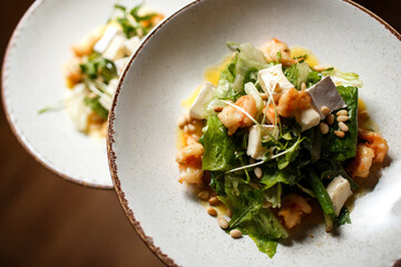 two salads with shrimps and cheese on white plates