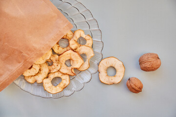 Paper bag with dried sliced apple chips and walnuts - healthy snacks on the plate. Top view. Proper nutrition, healthy food concept
