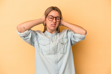 Young caucasian woman isolated on yellow background covering ears with hands.