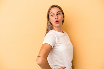 Young caucasian woman isolated on yellow background looks aside smiling, cheerful and pleasant.