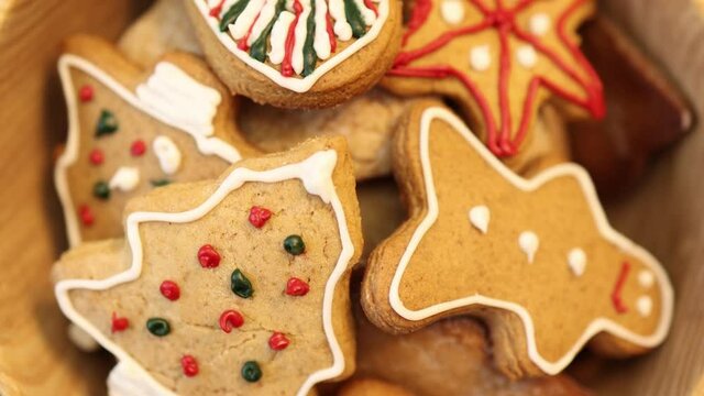 close-up view traditional Christmas cookies biscuits decorated with colorful glaze icing sugar. fir tree, gingerbread man, cane stick, star shape pastry rolling in wooden bow. winter holidays concept