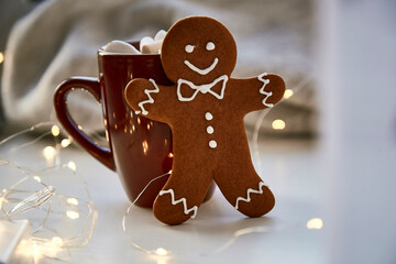 Symbol of Christmas - homemade gingerbread cookie and blurred bokeh decor. Festive Christmas decorations with hot drink and marshmallows. Aesthetic Christmas atmosphere, home coziness, warmth concept.