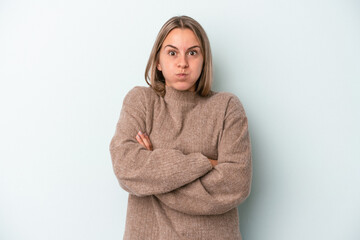 Young caucasian woman isolated on blue background blows cheeks, has tired expression. Facial...