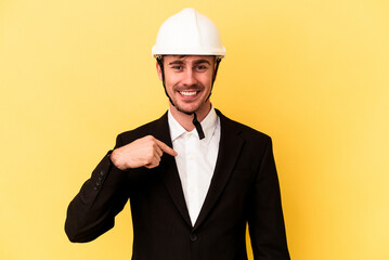 Young architect caucasian man isolated on yellow background person pointing by hand to a shirt copy space, proud and confident
