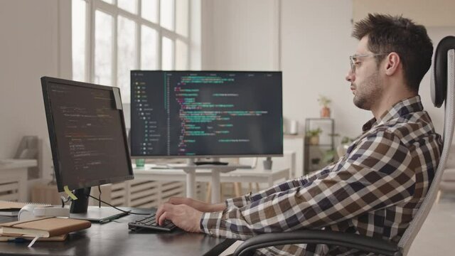 Side-view stab shot of professional system administrator or software developer writing program codes on pc computer working alone in modern office