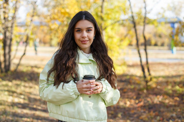 A joyful young woman with a cup of coffee in an autumn park