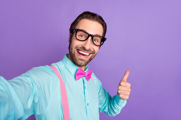 Photo of millennial brunet groomed guy show thumb up do selfie wear tie suspenders blue shirt eyewear isolated on purple background