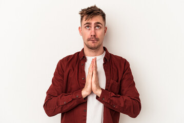 Young caucasian man isolated on white background holding hands in pray near mouth, feels confident.