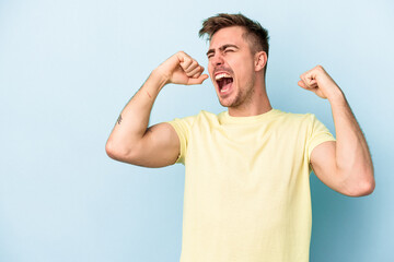 Young caucasian man isolated on blue background raising fist after a victory, winner concept.