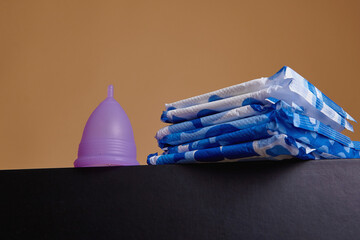 A silicone menstrual cup next to a stack of sanitary towels. Sustainability, zero waste, frugality concept. Alternative way to manage periods, menstrual cycles