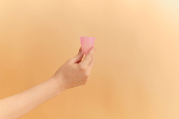 Close up of woman hand holding menstrual cup over color background. Women health concept, zero waste alternatives