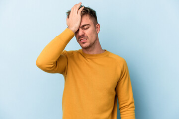 Young caucasian man isolated on blue background forgetting something, slapping forehead with palm...