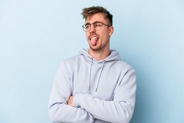 Young caucasian man isolated on blue background funny and friendly sticking out tongue.