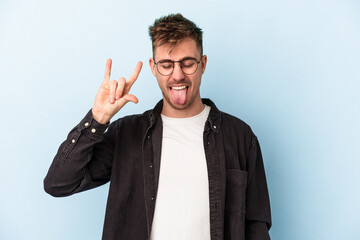 Young caucasian man isolated on blue background showing rock gesture with fingers