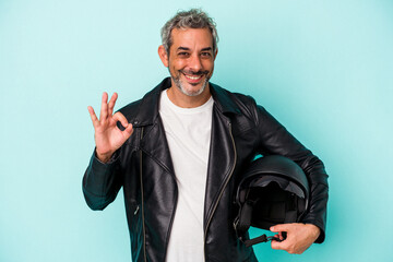 Middle age biker caucasian man holding helmet isolated on blue background  cheerful and confident...