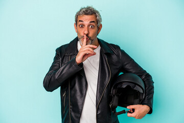 Middle age biker caucasian man holding helmet isolated on blue background  keeping a secret or...