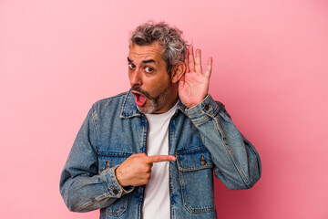 Middle age caucasian man isolated on pink background  trying to listening a gossip.