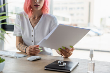 cropped view of pierced businesswoman with pink hair holding folder in office.