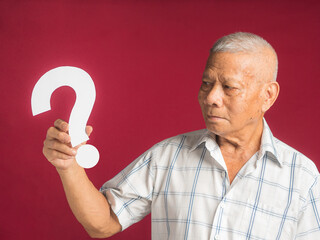 Question mark concept. Senior man holding and looking at a white question mark paper while standing with a red background in the studio. Close-up photo. Space for text