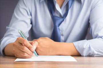 Close-up of a businessman holding a pen writing on paper on a wooden desk while sitting on a chair in the office. Space for text. Business and relaxation concept