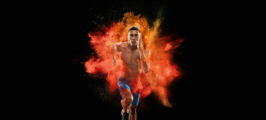 Creative portrait of young male athlete, sportive man running in explosion of colored neon powder isolated on dark background