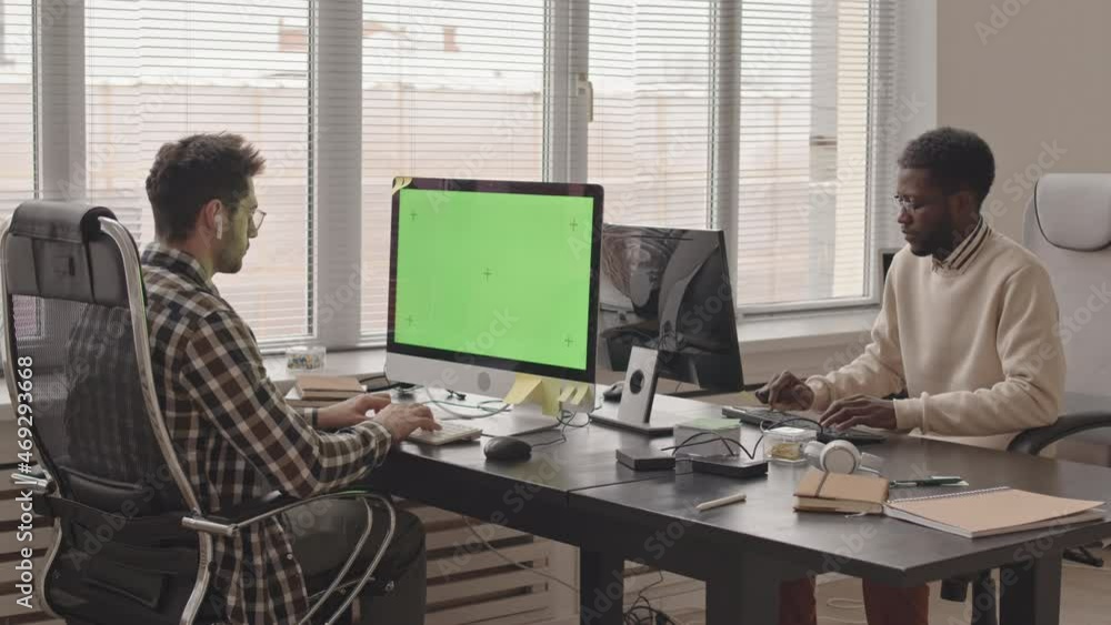 Wall mural stab shot with slowmo of two young multiethnic software engineers typing on keyboards looking at com