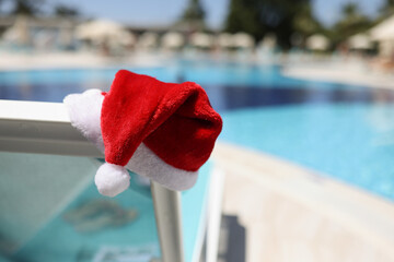 Santa claus hat put on lawn chair near swimming pool with clean turquoise water