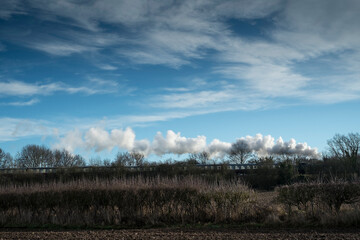 Fototapeta premium Steam train, partially hidden by trees, travels through the countryside, England, UK.
