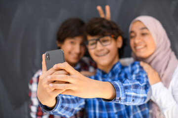 Group of arab teens taking selfie photo on smart phone with black chalkboard in background. Selective focus 
