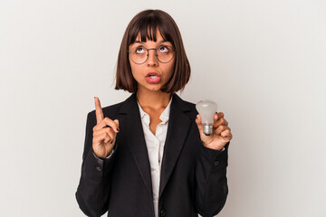 Young mixed race business woman holding a light bulb isolated on white background pointing upside with opened mouth.