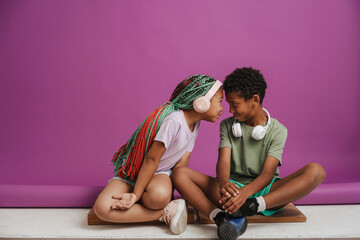 Black girl and boy with headphones smiling while sitting on floor