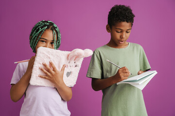 Black girl and boy writing down notes in exercise books together