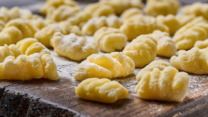 Homemade raw uncooked potato gnocchi with flour and grated parmesan cheese over wooden cutting board. Macro, selective focus