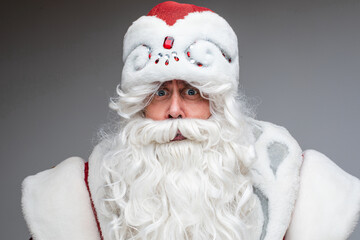Headshot of Santa Claus in red hat, gray-haired beared tired man on gray studio background