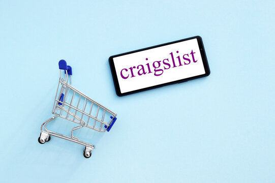 Shopping cart with a smartphone opened Craigslist logo on the screen on a blue background.